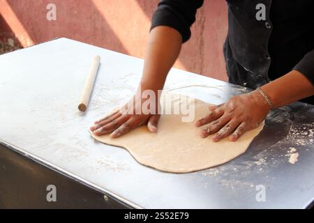 Hands of pizza maker man kneads dough, prepares and shapes for pizza base with rolling pin and flour Stock Photo
