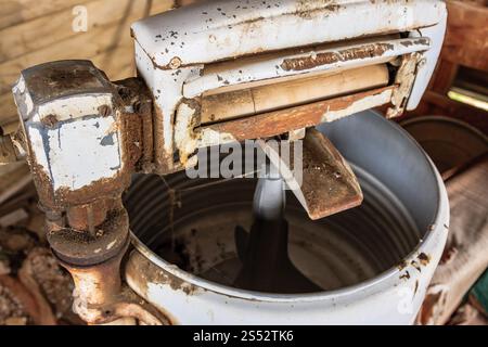An old, rusty washing machine sits in a dirty, cluttered room. The machine is covered in rust and dirt, and it is in disrepair. The room is filled wit Stock Photo