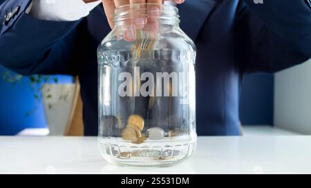 Closeup image of young businessman throwing coins in glass jar. Closeup photo of young businessman throwing coins in glass jar Stock Photo