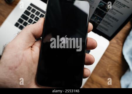 Paris, France - Mar 27, 2019: iPhone 16 Pro displaying the Apple logo and progress bar during startup, held in hand, with a MacBook Pro laptop visible Stock Photo