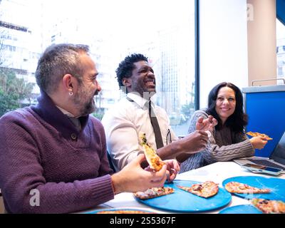Colleagues Laughing Over Pizza in a Bright Office Setting Stock Photo