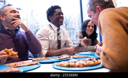 Diverse Team Laughing Over Pizza on a Rainy Day Stock Photo