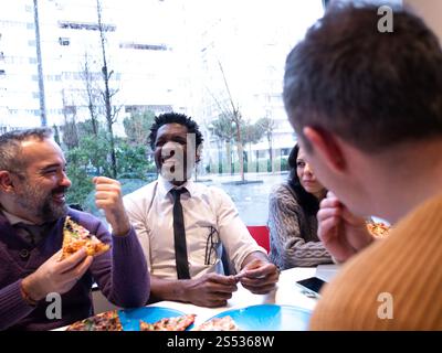 Colleagues Laughing Over Pizza in a Bright Office Setting Stock Photo