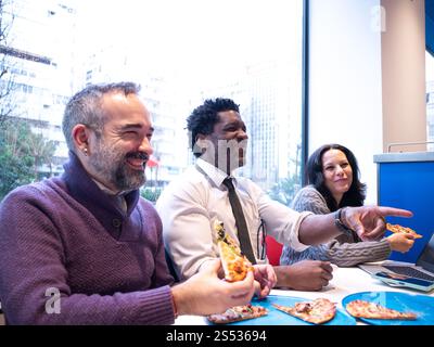 Colleagues Laughing and Pointing While Sharing Pizza Stock Photo