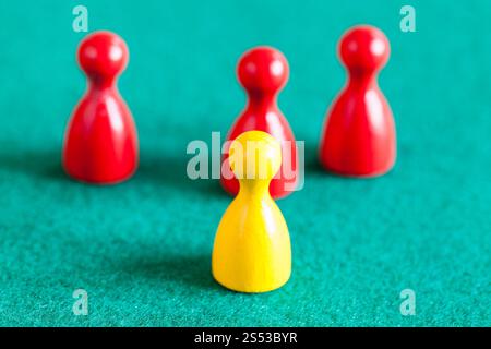 concept scene - one yellow pawn in front of three red pawns on green baize table. Focus on the yellow pawn Stock Photo