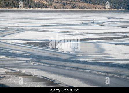 Snow patterns and two ice skaters on frozen Lake Minnewanka in Banff National Park Stock Photo