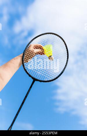 female hand strikes yellow shuttlecock by badminton racquet with background from blue sky with white clouds in sunny day (focus on the shuttlecock) Stock Photo