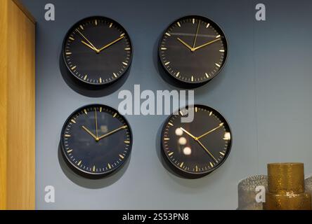 Multiple wall clocks displaying different times on a gray wall in a modern room Stock Photo