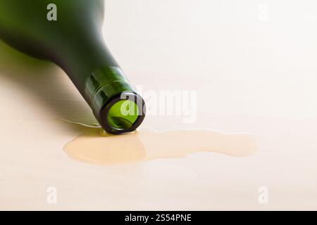 edge of cognac bottle in spilled liquid on wooden table close up. edge of cognac bottle in spilled liquid on table Stock Photo