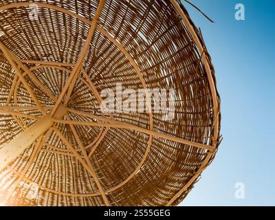 Photo of straw umbrellas on the ocean beach at hot sunny day against blue sky. Image of straw umbrellas on the ocean beach at hot sunny day against Stock Photo