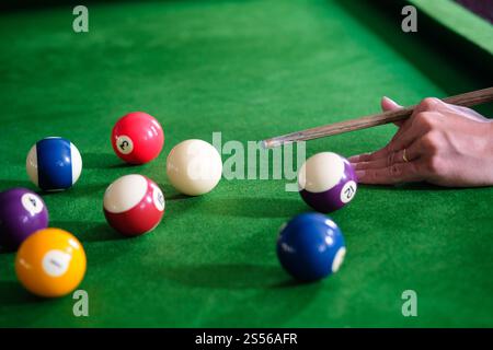 Mans hand and Cue arm playing snooker game or preparing aiming to shoot pool balls on a green billiard table. Colorful snooker balls on green frieze Stock Photo