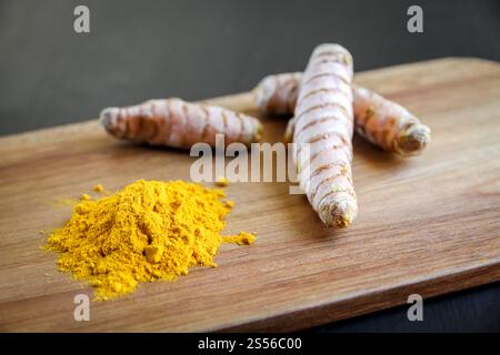 Turmeric root and spice powder on a wooden cutting board. Turmeric root and spice powder on a cutting board Stock Photo