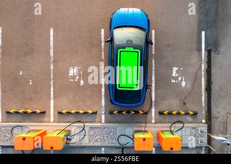 Electric car of blue color receives electricity for proper work of engine. Flashing green indicator on roof shows process of charging at station Stock Photo