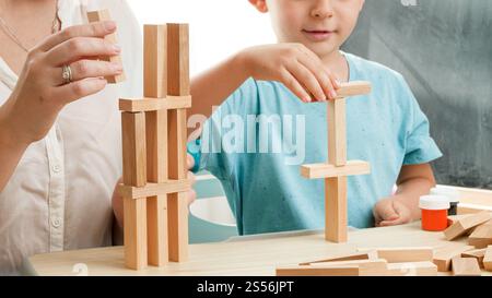 Smart boy with mother playing with wooden toy blocks and building high tower. Mother educating and teaching her child at home during lockdown and self Stock Photo