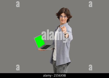 Young man holding modern laptop with green screen on grey background Stock Photo