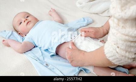 Young mother putting on new clean diapers on her little baby son lying on bed. Concept of parent,baby hygiene and child development. Stock Photo