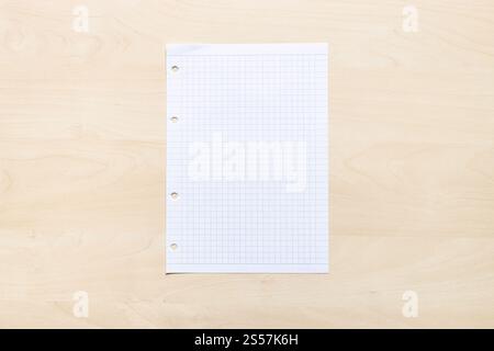 top view of blank sheet of squared paper on light brown wooden board Stock Photo