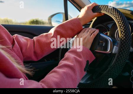 Businesswoman driving a modern car and using the buttons on the steering wheel while traveling on a sunny day Stock Photo