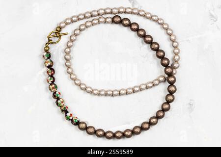 tangled handcrafted necklace from faceted nacre beads and hand-painted cloisonne beads with enamel on gray concrete board Stock Photo
