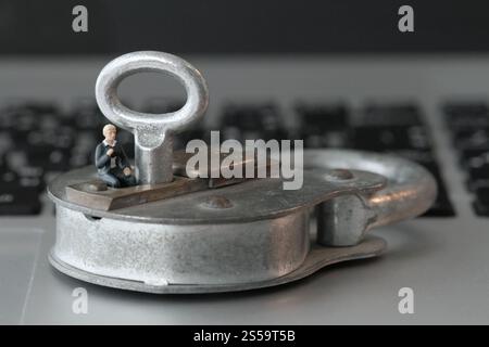 Internet security concept-miniature businessman sit on old key and padlock on laptop computer keyboard Stock Photo