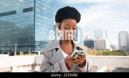 Smiling Woman Using Smartphone Outdoors in Urban City During a Bright Day Stock Photo