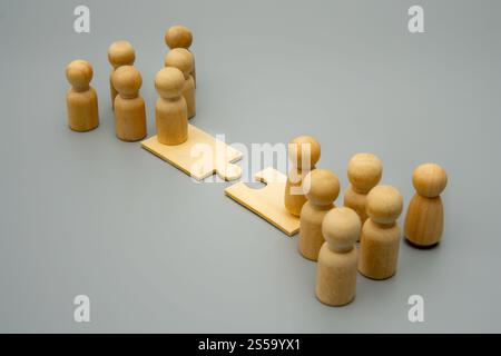 Two groups of wooden figures stand on opposite sides of a puzzle piece bridge. Mergers and acquisitions, business integration, and combining forces Stock Photo