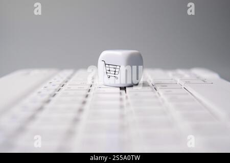A white die with a shopping cart symbol on a laptop keyboard. Online shopping, e-commerce, digital purchasing concept. Stock Photo