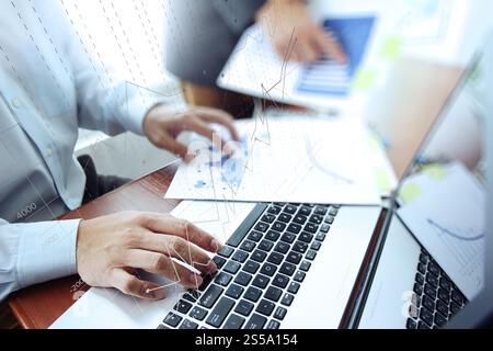 business documents on office table with laptop computer and two colleagues discussing data and graph business diagram in the background Stock Photo