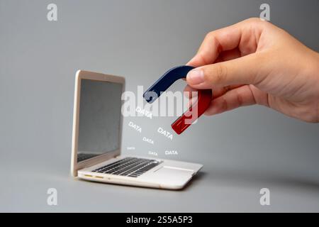 A hand holding a magnet near a laptop screen with the word "DATA". Data breaches and the vulnerability of digital information concept. Stock Photo