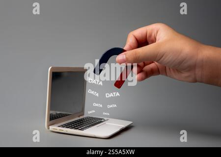A hand holding a magnet near a laptop screen with the word "DATA". Data breaches and the vulnerability of digital information concept. Stock Photo
