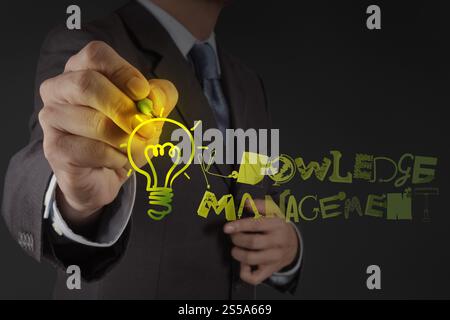 businessman hand drawing light bulb with design word KNOWLEDGE MANAGEMENT on virtual screen computer as concept Stock Photo
