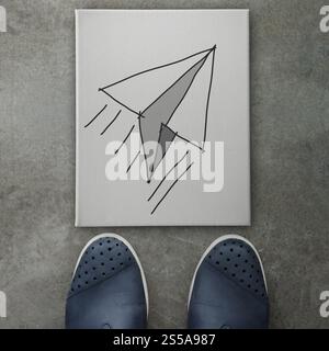 Hand drawn paper plane icon on canvas board on front of business man feet as concept Stock Photo
