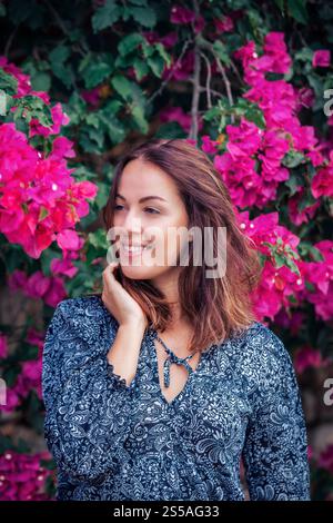 young brunette woman wearing a floral pattern summer dress, next to colorful blooming bushes, on Mallorca Stock Photo