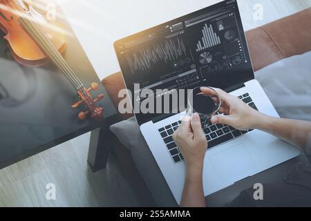 hipster hand holding a cup of coffee while composing music with laptop compter and sitting on sofa at home studio Stock Photo