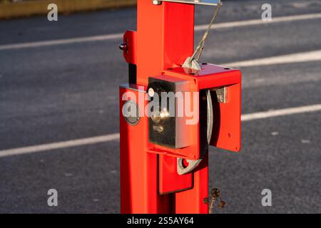 A bright red gate mechanism is affixed to a sturdy post, resting on a paved area. The device features various components and panels, showcasing its functional design in natural light. Stock Photo