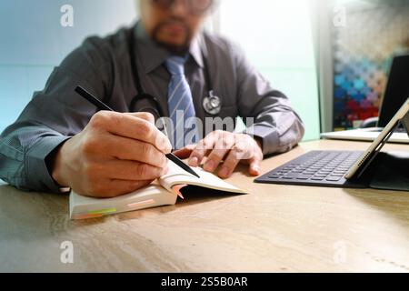 medical doctor writing on notebook and digital tablet docking keyboard with laptop on marble desk,sun flare effect Stock Photo