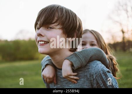 Happy family portrait. Brother holds his younger sister behind his back, they have fun and laugh. Stock Photo