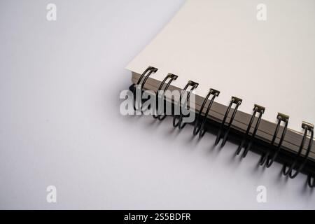 close-up of a spiral-bound notebook with blank pages.The focus is on the spiral binding and the edge of the paper, set against a minimalist background Stock Photo