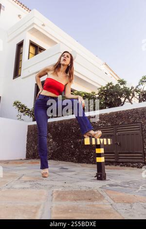 A woman with confidence in a red top and blue jeans poses outdoors. Stock Photo