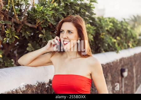 A happy woman in a red dress is talking on her cell phone, she is enjoying the conversation. Stock Photo