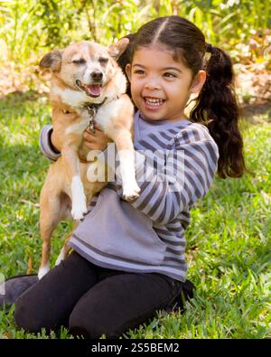 Smiling girl sitting on a lawn holding her pet terrier dog Stock Photo