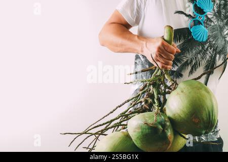 Summer and holiday fashion concept.Man Wearing palm trees graphics on T-shirt and holding cluster of coconuts with items on white background Stock Photo