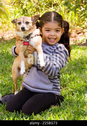 Smiling girl sitting on a lawn in summer holding her pet terrier dog Stock Photo