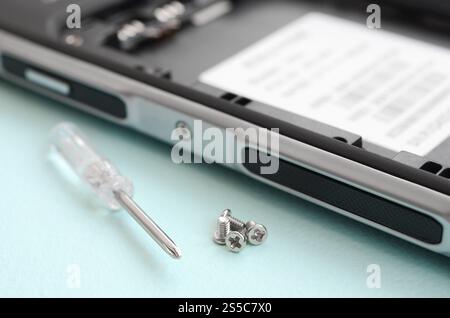 A small screwdriver and a few screws on a blue background. Tools for the repair and disassembly of modern smartphones and mobile devices. Tools for Stock Photo