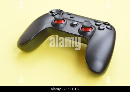Modern black video game controller on yellow background close up. Online video game players community concept. Modern black video game controller on Stock Photo