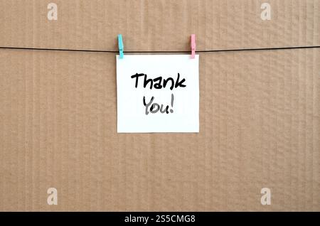Thank you! Note is written on a white sticker that hangs with a clothespin on a rope on a background of brown cardboard Stock Photo