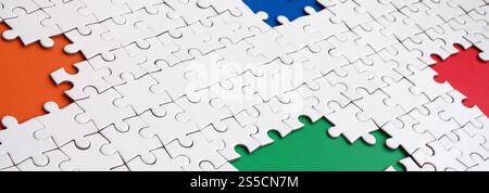 Close-up texture of a white jigsaw puzzle in assembled condition with missing elements, under which surfaces of different colors Stock Photo