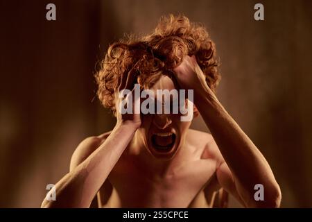 Medium close up of young adult man holding head while depressed crying Stock Photo