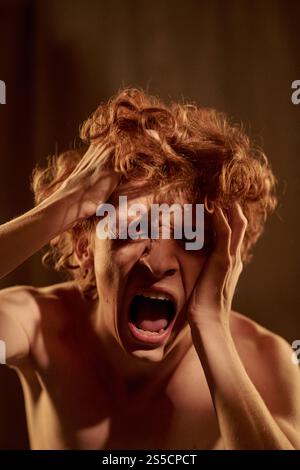 Vertical shot of young adult man crying because having strong headache Stock Photo