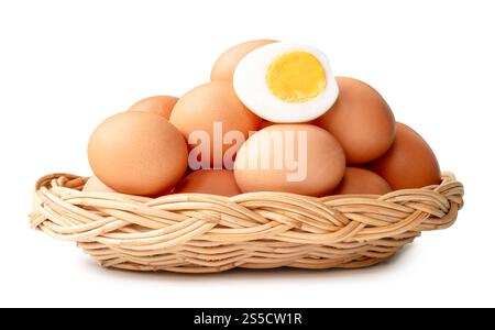 Large group of raw brown chicken eggs and peeled cooked or boiled eggs with egg yolk in half in stack in wicker basket is isolated on white background Stock Photo